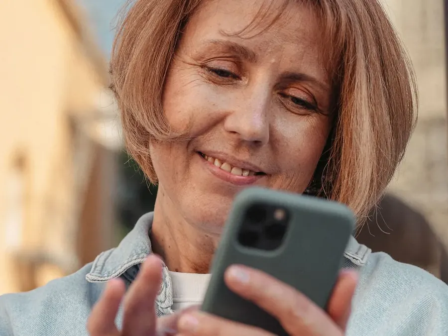 Imagen referencial: mujer sonriendo mientras revisa su celular